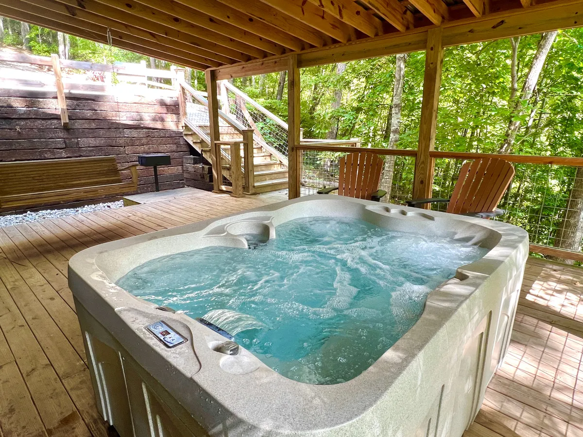 This exterior image showcases the hot tub, wooden deck, and a swing bench nestled among greenery. The swing bench invites gentle relaxation, while the deck offers ample space for socializing or soaking in the evening air under a canopy of trees.
