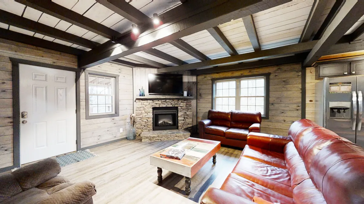 A cozy living room scene with red leather sofas arranged around a stone fireplace and a wooden coffee table, with a TV mounted on the wall. The setup is ideal for movie nights, game nights, or relaxing by the fire, creating an atmosphere of comfort and connection.