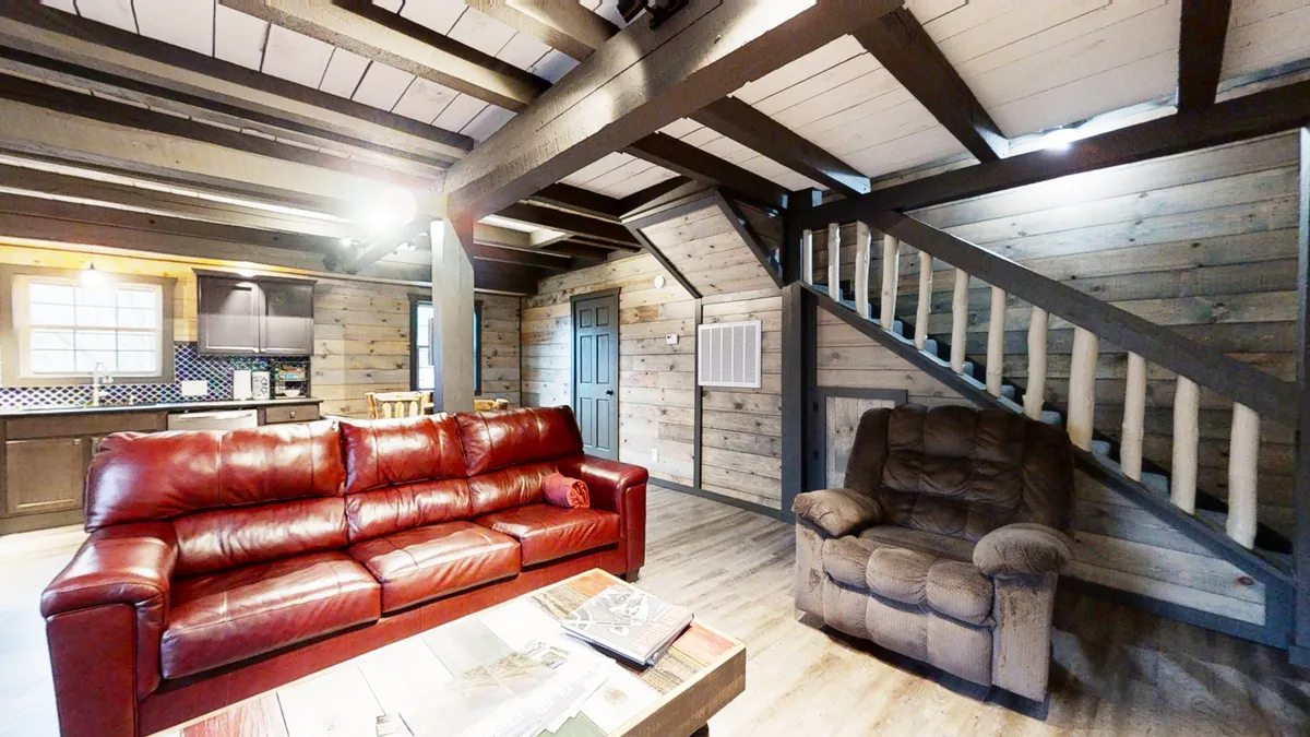 A welcoming living area featuring a red leather sofa, wooden staircase, and kitchen area in view. The space is arranged for relaxation, lively conversation, and quiet moments, suitable for various family members.
