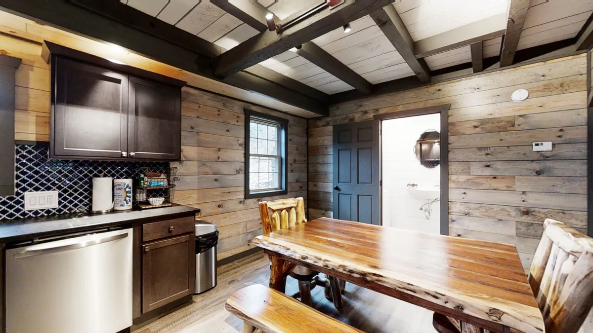 A warm, rustic dining area with a wooden table, cabinets, a window, and a door. The scene evokes shared meals and family gatherings, perfect for game nights or cooking together after a day of exploring.
