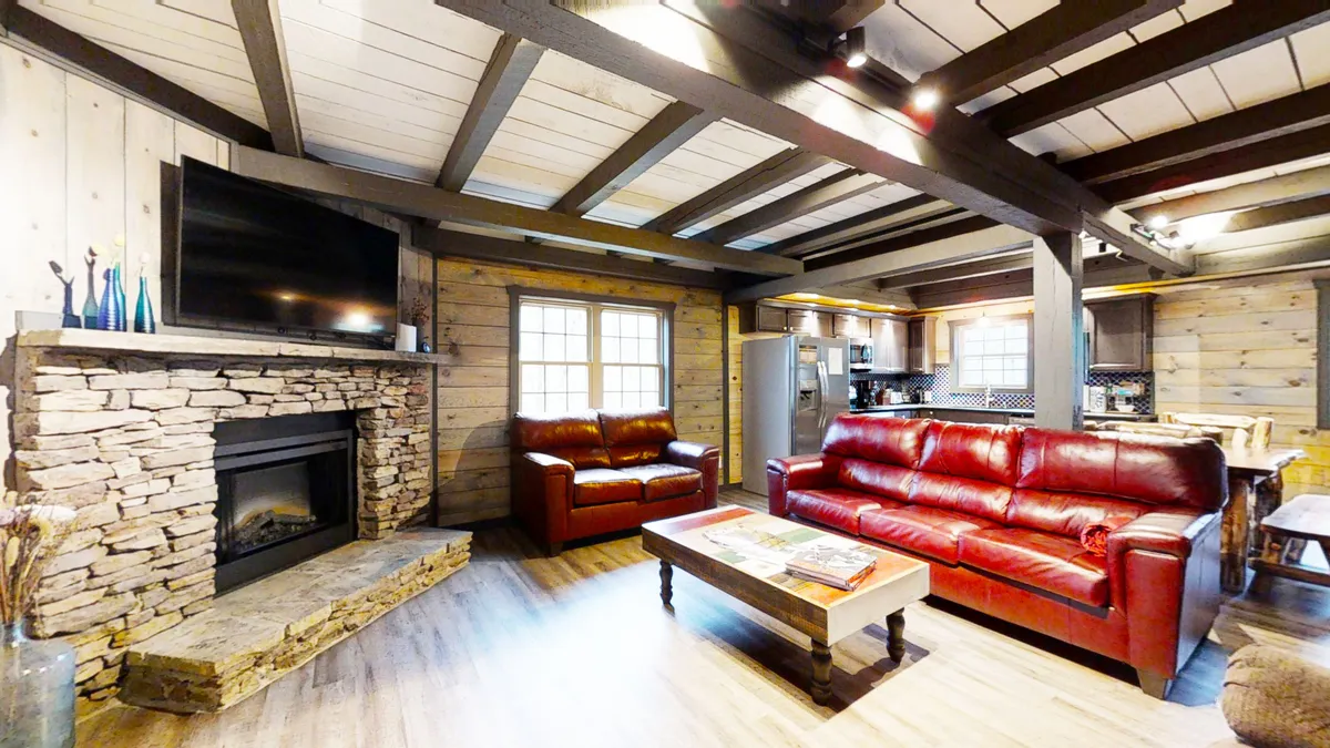 A spacious, warm interior living room with a prominent stone fireplace, plush red leather sofas, wooden beams, and a central coffee table. The atmosphere is perfect for entertaining, group gatherings, and cozy evenings.