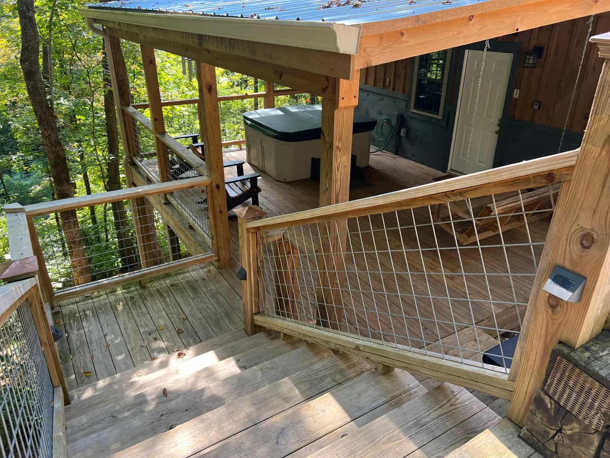 This exterior image captures the private deck surrounded by lush trees, featuring a prominent hot tub and comfortable outdoor seating. The scene is tranquil, with the wooden deck blending seamlessly with its natural surroundings, inviting guests to relax and enjoy the peaceful atmosphere.