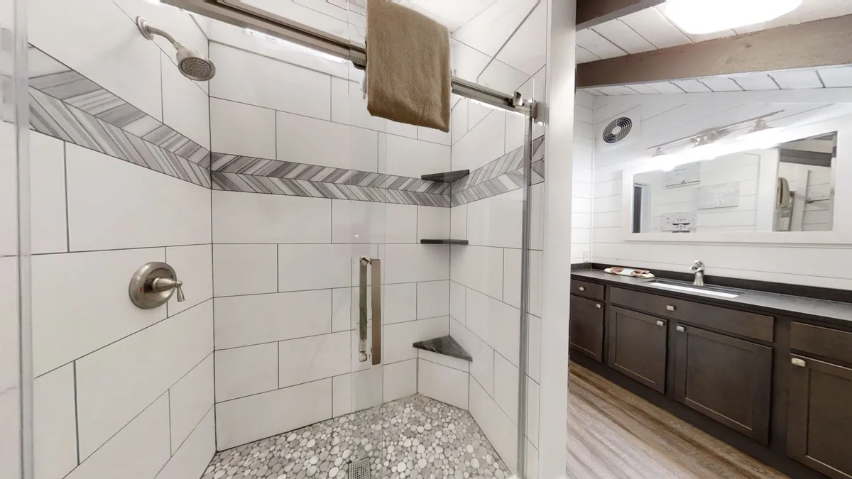 A beautifully tiled walk-in shower with a herringbone design and stone flooring is the centerpiece, signaling a fresh and tranquil ensuite bath experience. The shower area feels modern and rejuvenating, perfect for relaxing after a long day.